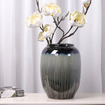 Un vase en céramique de couleur verte foncée contenant de belles fleurs blanches aux pétales délicats sur une table blanche.