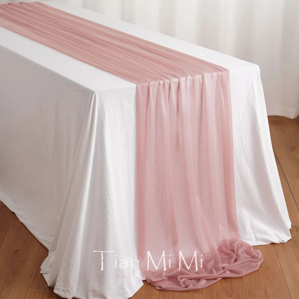 Cette nappe de table en satin rose délicatement drapée sur un sol en bois crée une ambiance élégante et féminine.