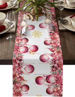 Table de fête décorée de décorations de Noël en rose et de bougies, sur un chemin de table à motifs de boules de Noël rose et de fleurs roses.