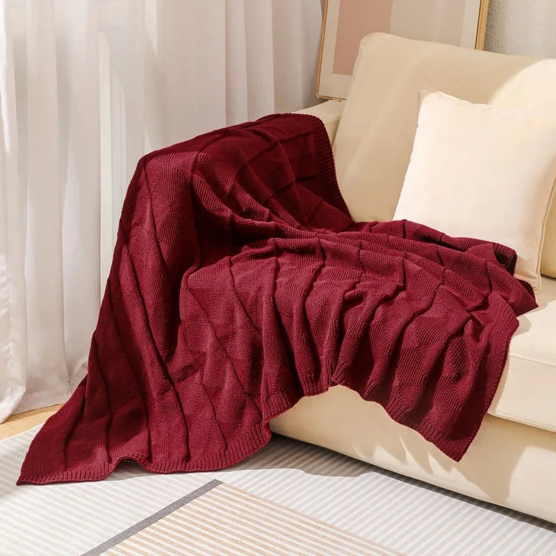 Une couverture en tricot rouge bordeaux décorative posée sur un canapé blanc, créant une ambiance chaleureuse et confortable dans l'espace.