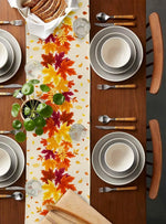 Une table de salle à manger élégamment dressée avec des assiettes, des couverts et des feuilles d'automne colorées, créant une atmosphère chaleureuse et conviviale.