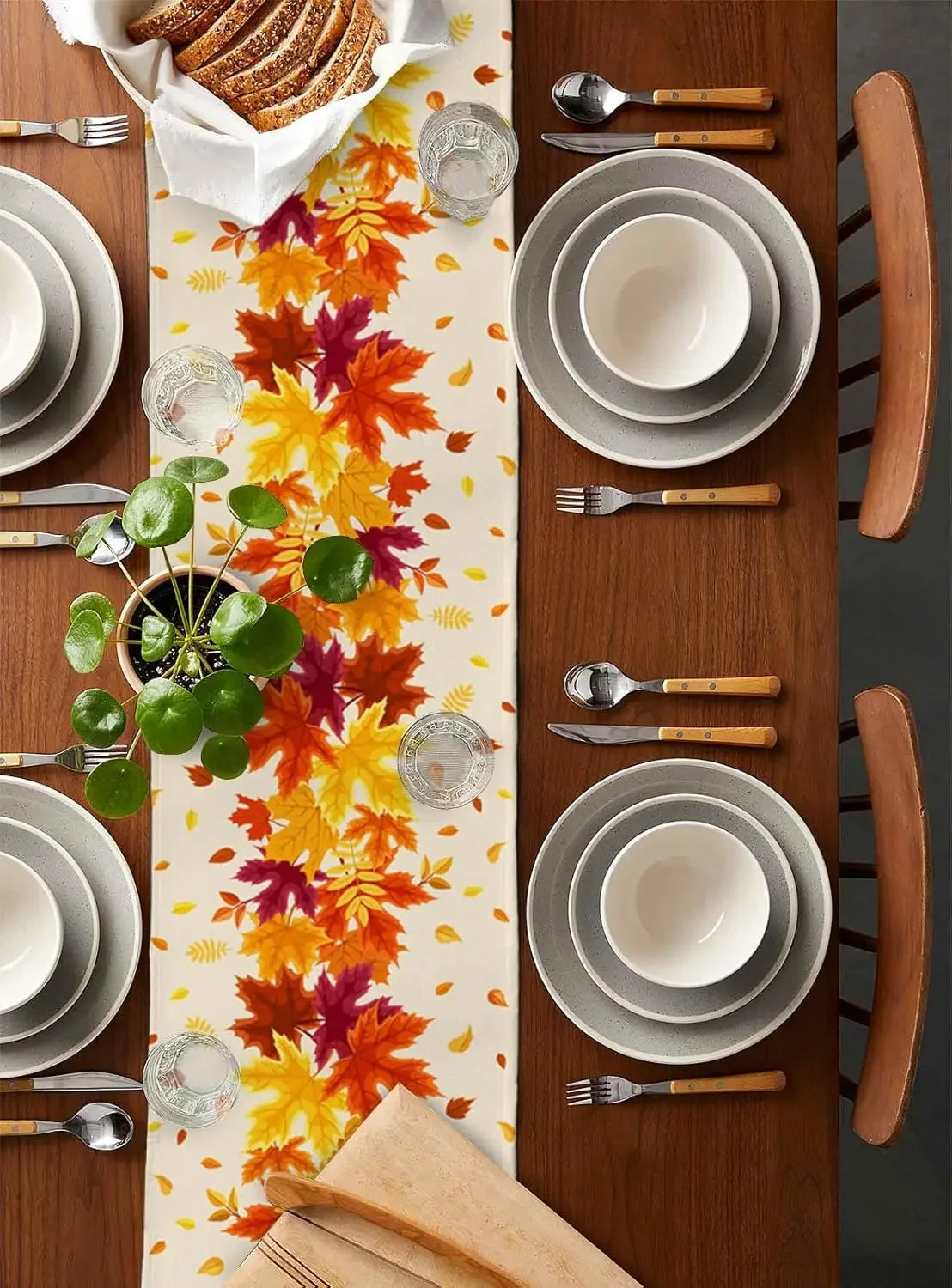 Une table de salle à manger élégamment dressée avec des assiettes, des couverts et des feuilles d'automne colorées, créant une atmosphère chaleureuse et conviviale.