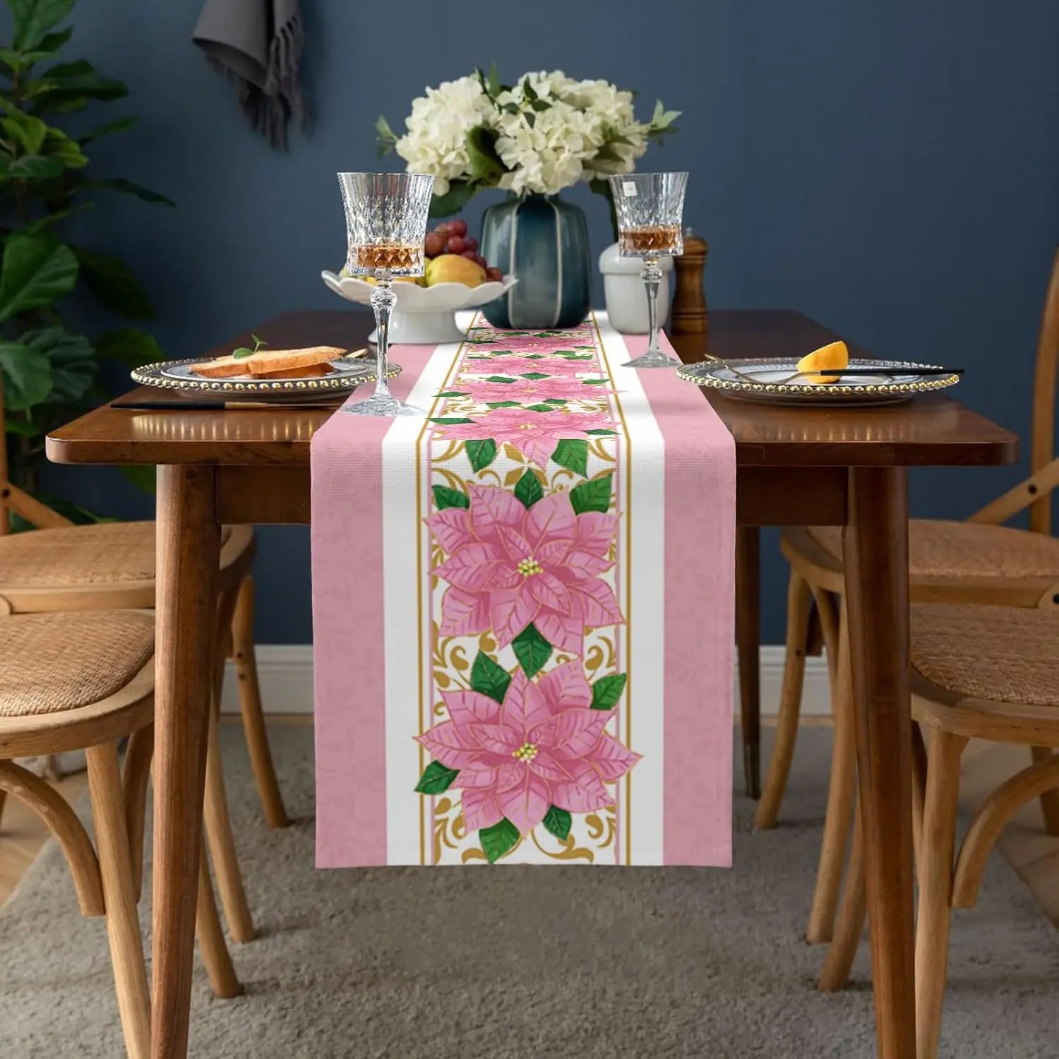 Cette image présente une table dressée avec élégance, ornée d'un chemin de table rose et fleuri, de verres sophistiqués et de bouquets de fleurs blanches. Elle dégage une atmosphère chaleureuse et festive.