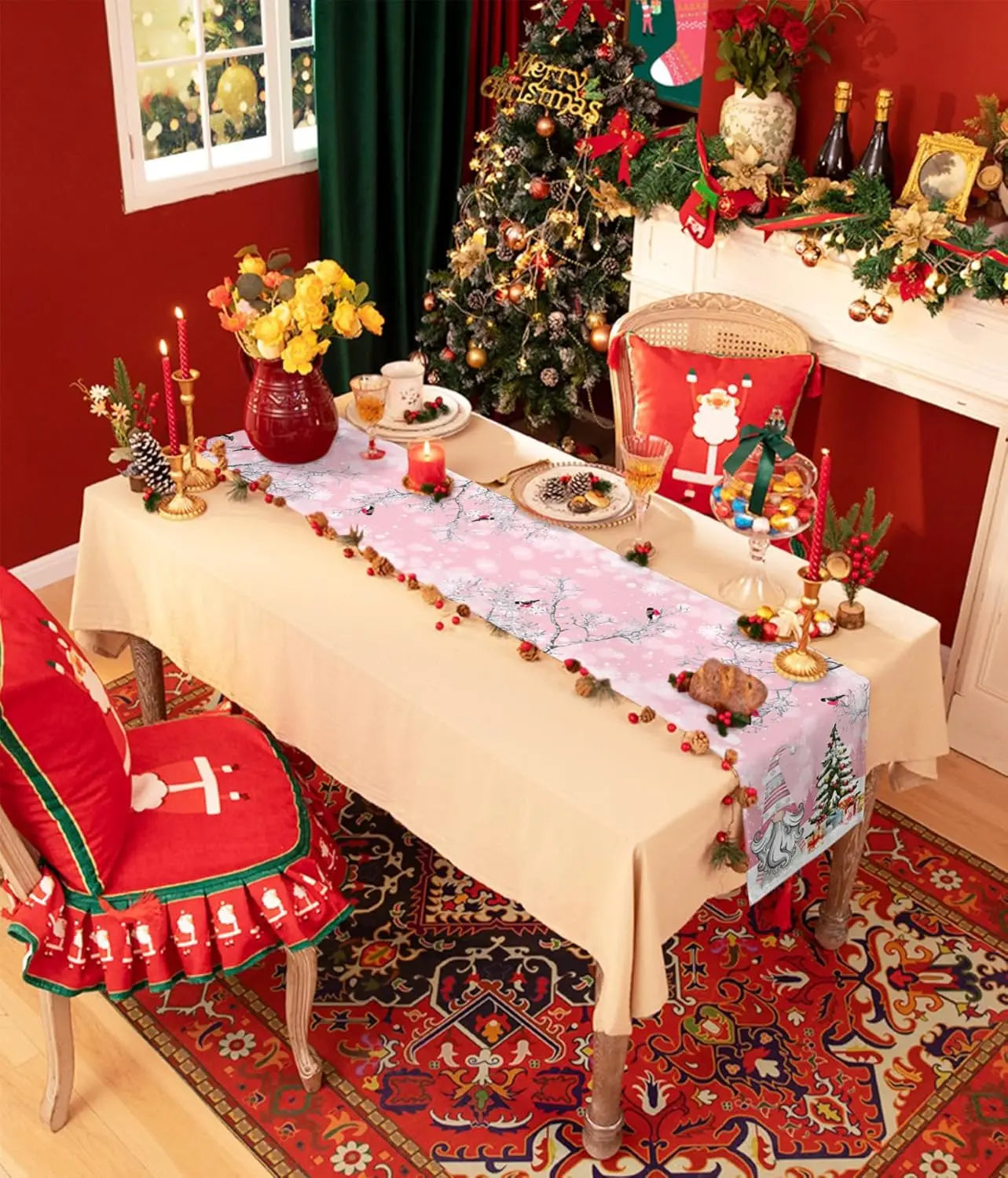 Une décoration de Noël festive et colorée avec un sapin, des ornements, des bougies et une nappe ornée d'un motif hivernal décorant une table dans une pièce aux murs rouges.