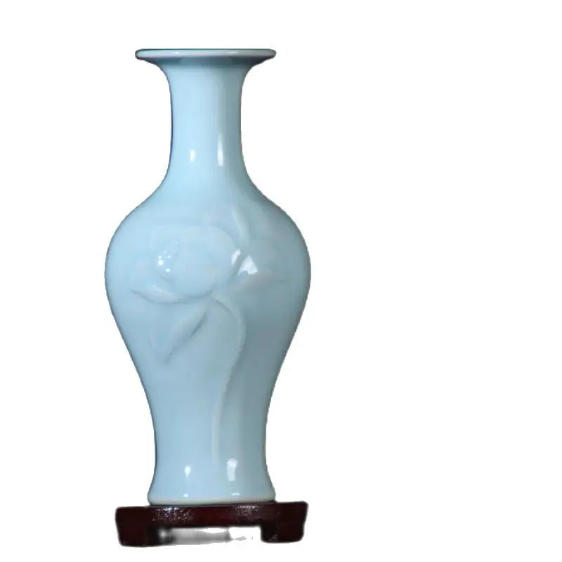 Un vase élégant et brillant de couleur bleu clair, avec une forme galbée et épurée, posé sur un socle sombre en bois.