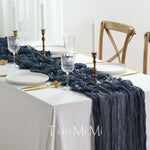 La table est soigneusement mise avec des assiettes blanches, des verres de cristal, des couverts dorés et une nappe blanche ornée d'un chemin de table en satin gris foncé, créant une ambiance élégante et raffinée.