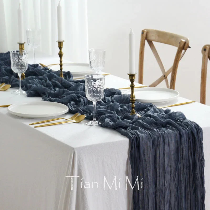 Une élégante table dressée avec des assiettes blanches, des verres de cristal, des chandeliers dorés et une nappe en tissu froissé gris, créant une atmosphère chic et raffinée.