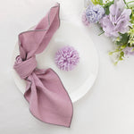 Sur une assiette blanche repose une belle serviette de table rose nouée en nœud, accompagnée de fleurs violettes fraîches.