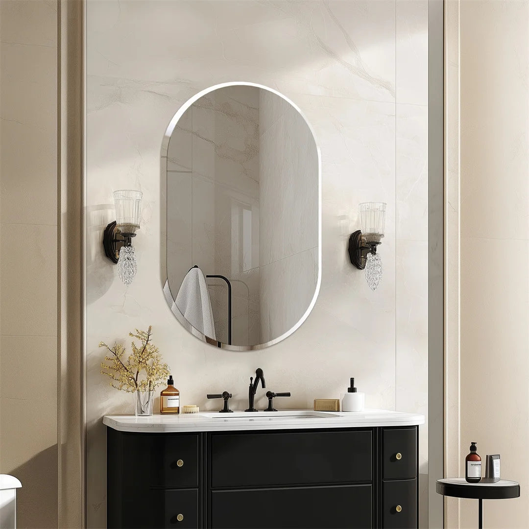 Ce miroir ovale élégant avec des appliques en cristal crée une ambiance chaleureuse et sophistiquée dans cette salle de bain contemporaine aux teintes neutres.