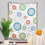 Tapisserie murale colorée et vibrante avec des motifs de fleurs géométriques stylisées dans des tons de bleu, vert et orange sur un fond blanc cassé.