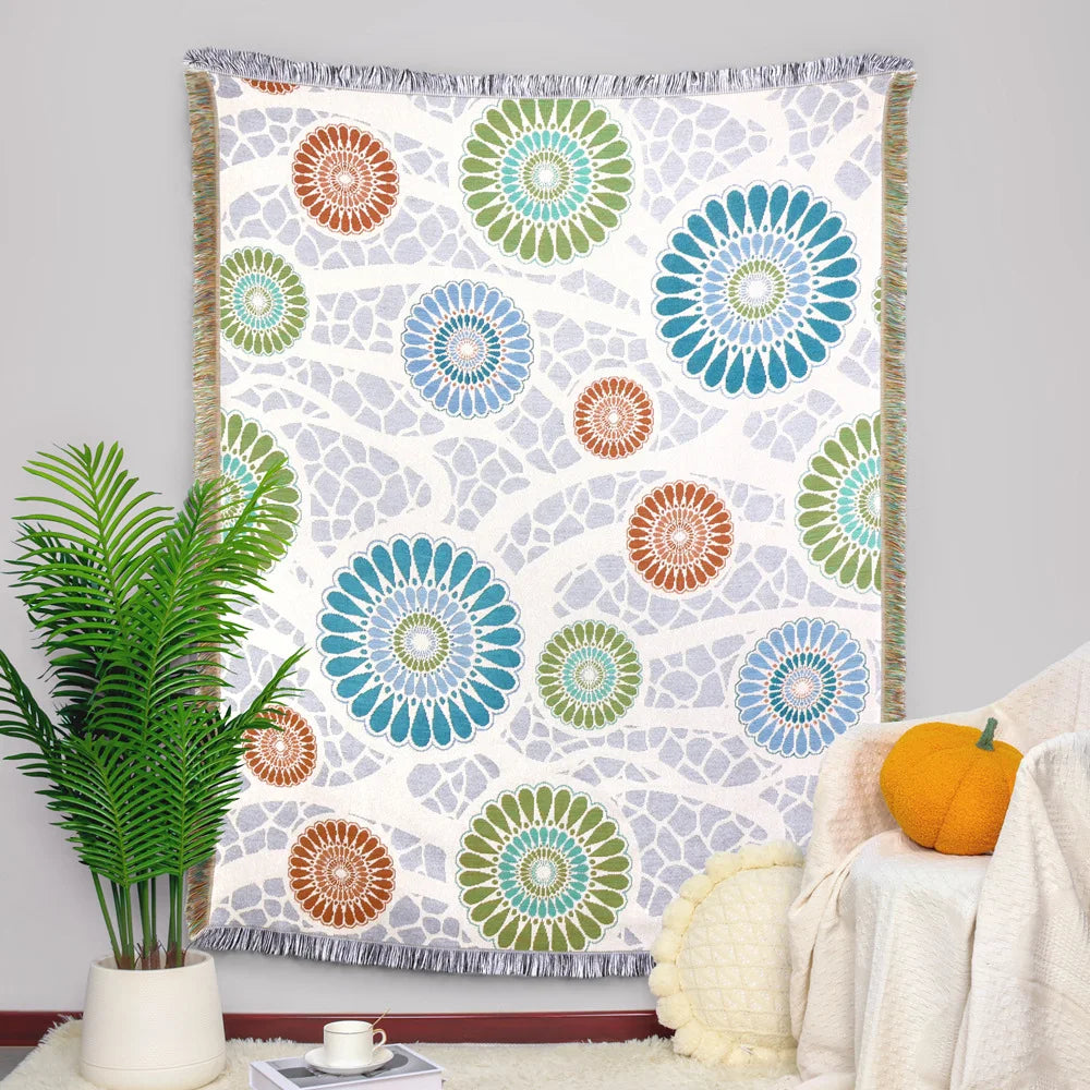 Tapisserie murale colorée et vibrante avec des motifs de fleurs géométriques stylisées dans des tons de bleu, vert et orange sur un fond blanc cassé.
