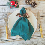 Une nappe de Noël avec une serviette enroulée et décorée de cônes de pin et de baies rouges sur une table en bois.