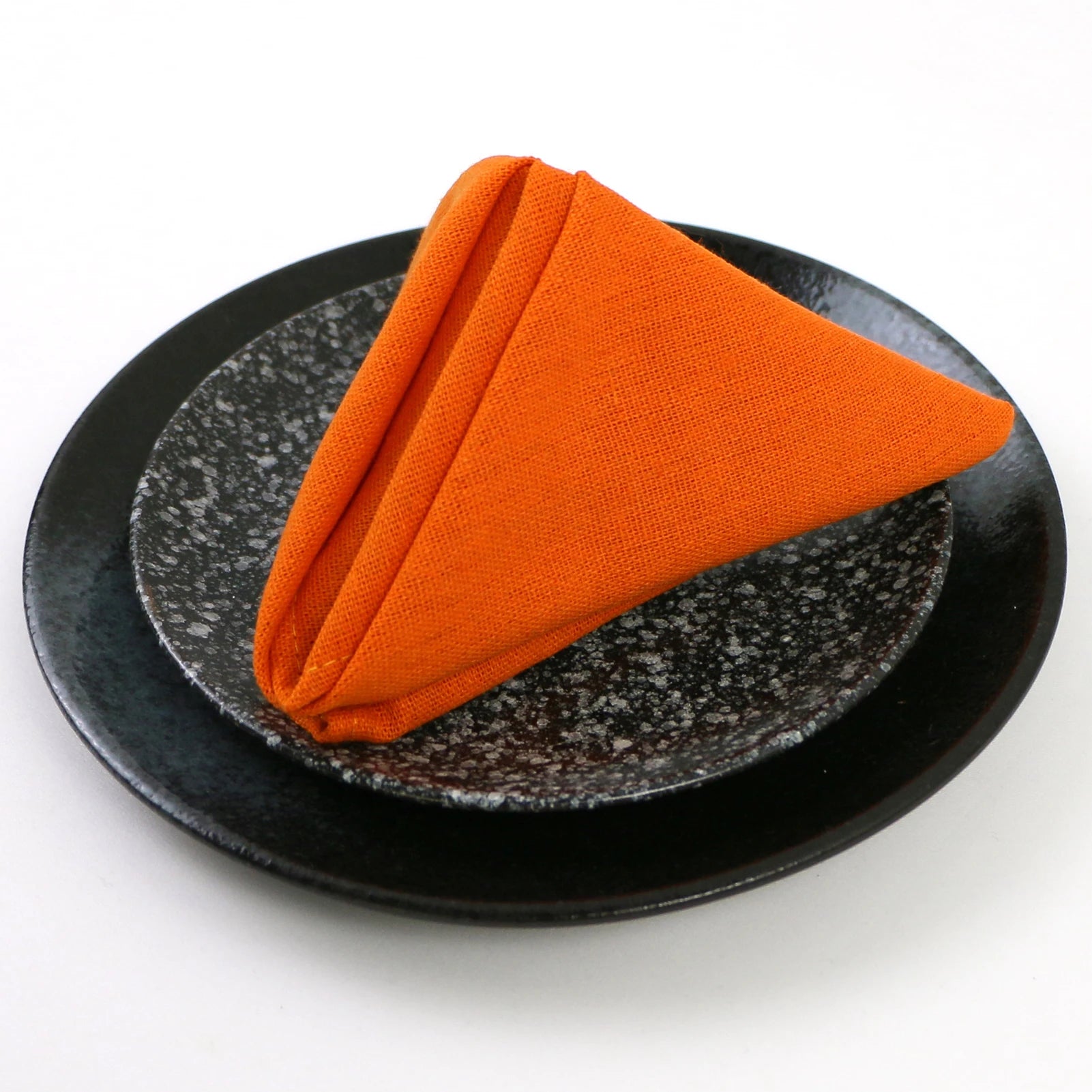 Un tissu orange vif, plié de manière élégante sur une assiette noire texturée.