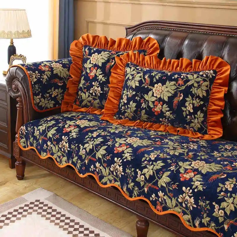 Cette image montre un canapé en cuir brun avec des coussins fleuris bleus et oranges, ainsi qu'un plafonnier blanc et des décorations murales, créant une ambiance élégante et chaleureuse dans la pièce.