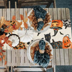 Une scène d'automne festive avec des éléments décoratifs orange et noir, incluant des citrouilles, des chauves-souris et un chat noir.