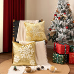 Une pièce accueillante décorée pour les fêtes, avec un sapin de Noël enneigé, des coussins dorés ornés de flocons de neige et des cadeaux emballés sous l'arbre.