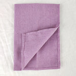 Couverture tricotée en laine de couleur lilas, pliée sur un fond blanc.