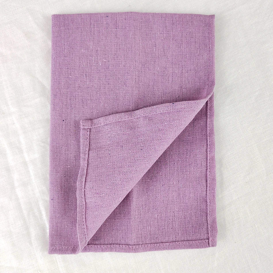 Couverture tricotée en laine de couleur lilas, pliée sur un fond blanc.