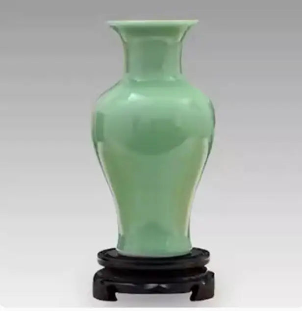 Vase en céramique de couleur vert clair posé sur un support en bois sculpté.
