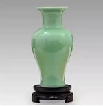 Vase en céramique de couleur vert clair posé sur un support en bois sculpté.