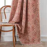 Rideau fleuri vintage avec pompons, en tissu jacquard rose et beige, tombant élégamment sur une chaise en bois dans un intérieur au style rétro et naturel.