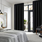 Rideaux noirs occultants posés dans une chambre moderne avec lit gris, baie vitrée et accès à un balcon verdoyant.