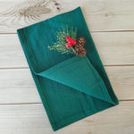 Un journal relié en vert orné de pommes de pin et de baies rouges, décoré sur une surface en bois.