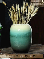 Un vase de céramique vert émaillé rempli de tiges de blé doré, créant une composition naturelle et élégante.