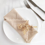 Une nappe beige en lin avec un bouquet de fleurs séchées est posée sur une assiette blanche avec une fourchette et un couteau en métal.