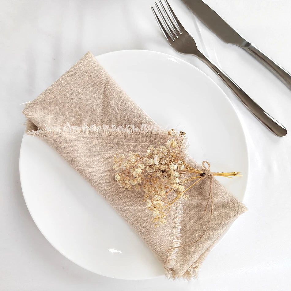 Une nappe beige en lin avec un bouquet de fleurs séchées est posée sur une assiette blanche avec une fourchette et un couteau en métal.