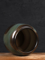 Un vase vintage en céramique, aux teintes de vert, de brun et de dorée, posé sur une surface en bois.