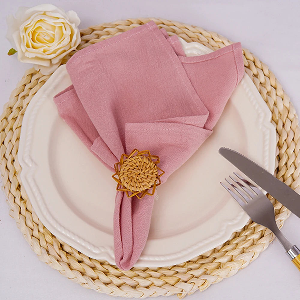 Arrangement élégante de table avec serviette rose, fleur décorative dorée et couverts sur un napperon en paille tressé.