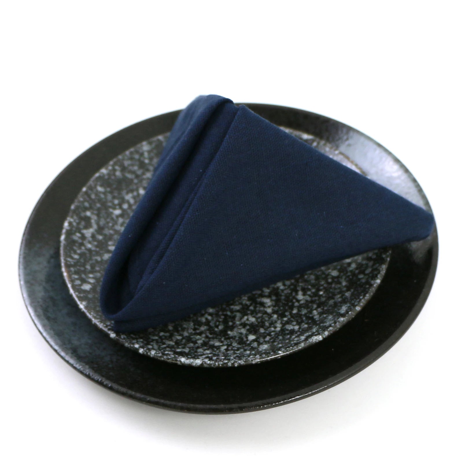 Un serviette bleue marine pliée se trouve sur une assiette en céramique noire texturée.