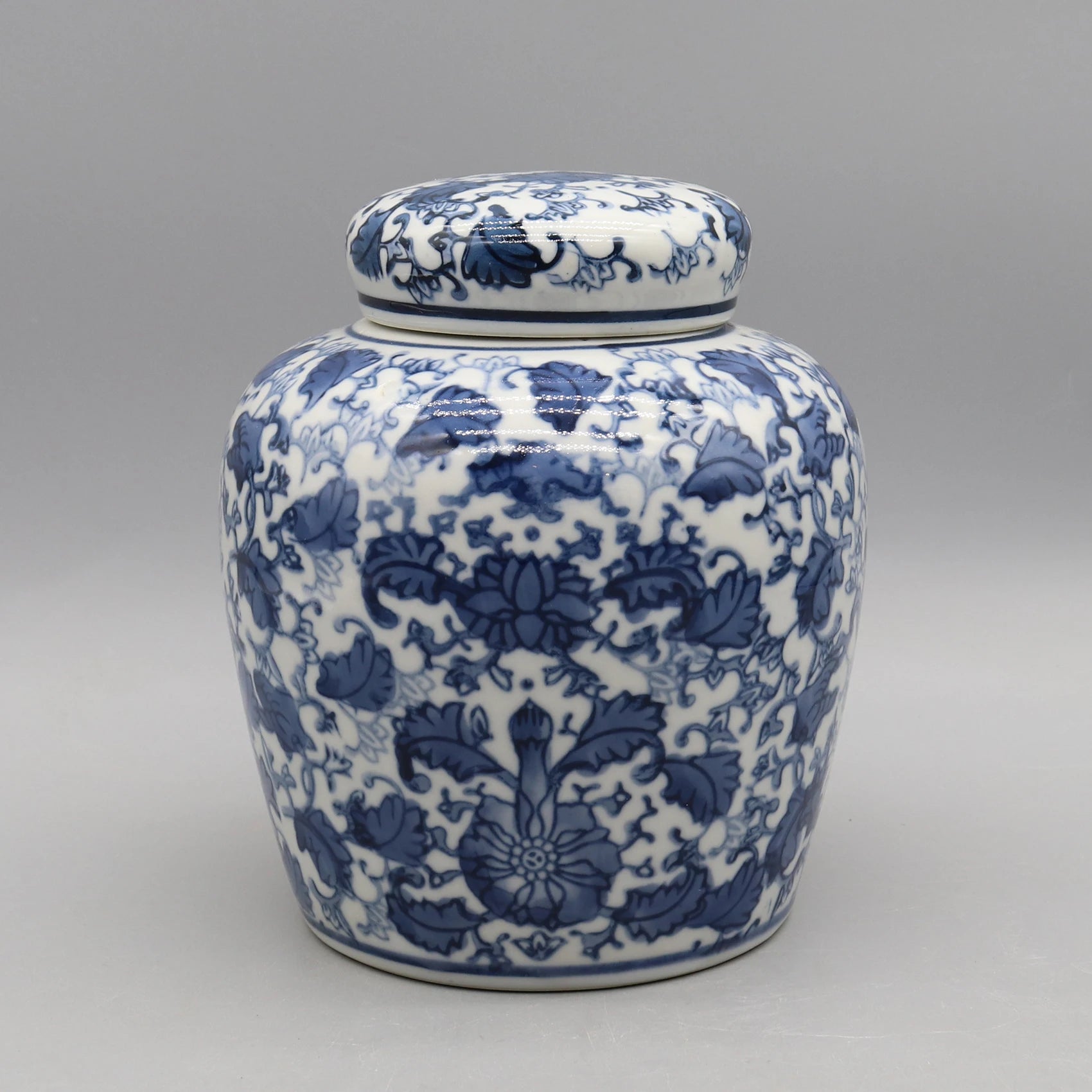 Pot de porcelaine décoré de motifs floraux bleus et blancs sur un fond gris neutre.