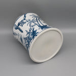 Cette image montre un pot en céramique blanc orné de motifs bleus représentant des feuilles de palmiers, des plantes et des oiseaux.