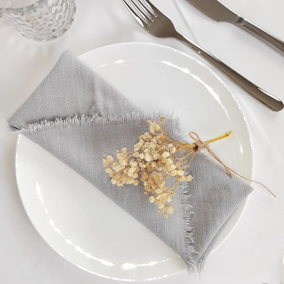 Une serviette de table grise avec un bouquet de fleurs séchées attaché avec de la ficelle sur une assiette blanche, à côté d'une fourchette et d'un couteau.
