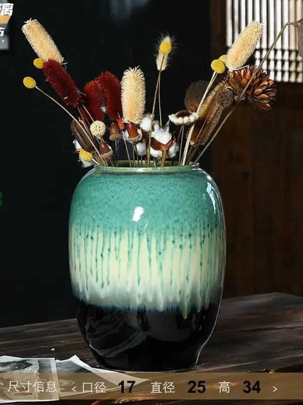 Un vase en céramique aux couleurs vertes et noires, rempli de fleurs et de tiges séchées aux tons chauds, créant une belle composition rustique et naturelle.