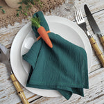 Une nappe de table en tissu vert foncé avec un morceau de carotte en forme de décoration posé sur une assiette blanche, accompagné de couverts en bois.