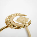 Bague dorée ornée de motifs décoratifs sculptés avec un élément central en forme de lune.
