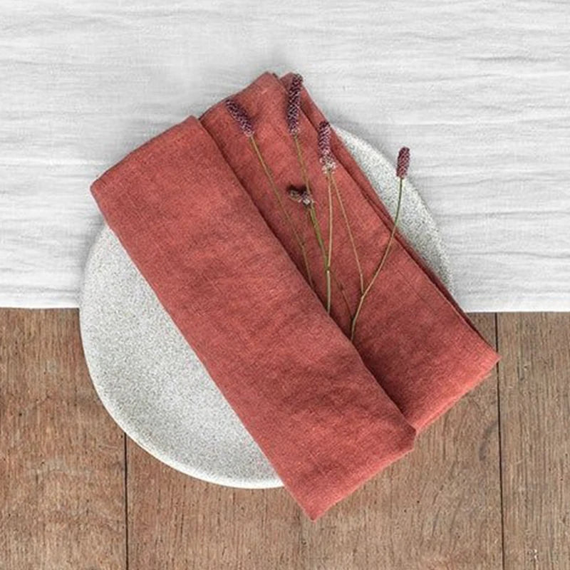 Ensemble de serviettes de table rouges sobre et élégant, posé sur un support en bois et un fond blanc, représentant une décoration de table de style épuré et naturel.