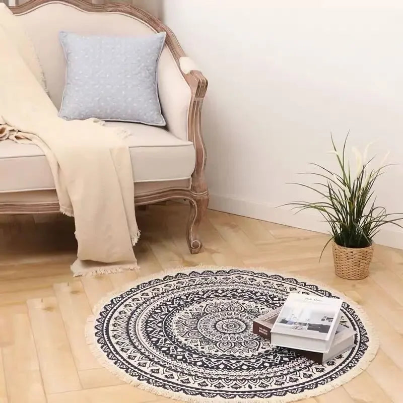 Tapis rond ornemental de style bohème avec motifs ethniques noirs et blancs, placé sur le sol à côté d'un fauteuil vintage et d'un pot de plante verte.