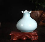 Un vase en céramique bleu pâle avec des détails sculptés, posé sur un support en bois foncé.