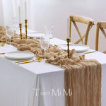 Une table élégante, avec une nappe blanche, des accessoires dorés et un chemin de table en tissu froissé, crée une ambiance chic et raffinée pour un repas.