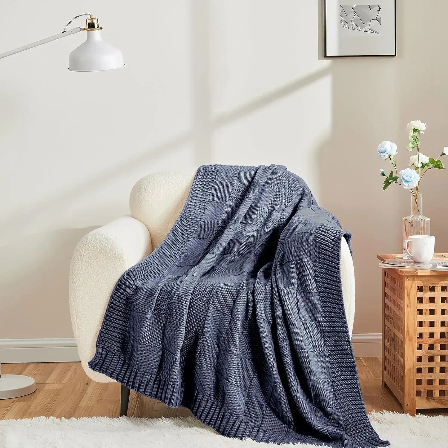 Une couverture tricotée grise reposant sur un fauteuil moelleux, créant une ambiance cosy et apaisante dans cette pièce lumineuse.