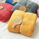 Une pile de couvertures en tissu colorées et douces, attachées avec des étiquettes en carton. Les couleurs vives et le style texturé créent un look moderne et accueillant.
