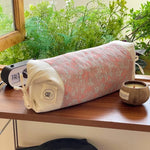Un rouleau de yoga coloré et décontracté, entouré de plantes vertes épanouies, suggère un environnement serein et apaisant pour la pratique du yoga.