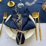 Un couvert élégant sur fond bleu marine, avec des couverts dorés et une serviette de table décorée de fleurs séchées, créant une ambiance chic et raffinée.
