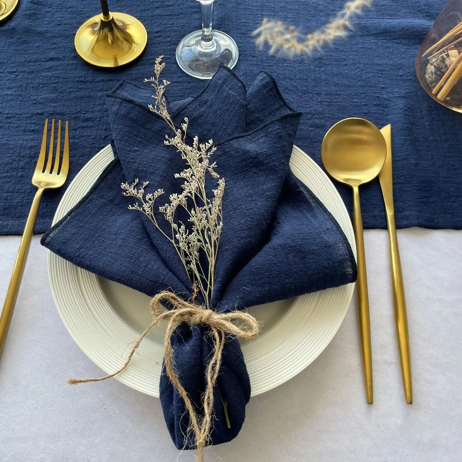 Un couvert élégant sur fond bleu marine, avec des couverts dorés et une serviette de table décorée de fleurs séchées, créant une ambiance chic et raffinée.