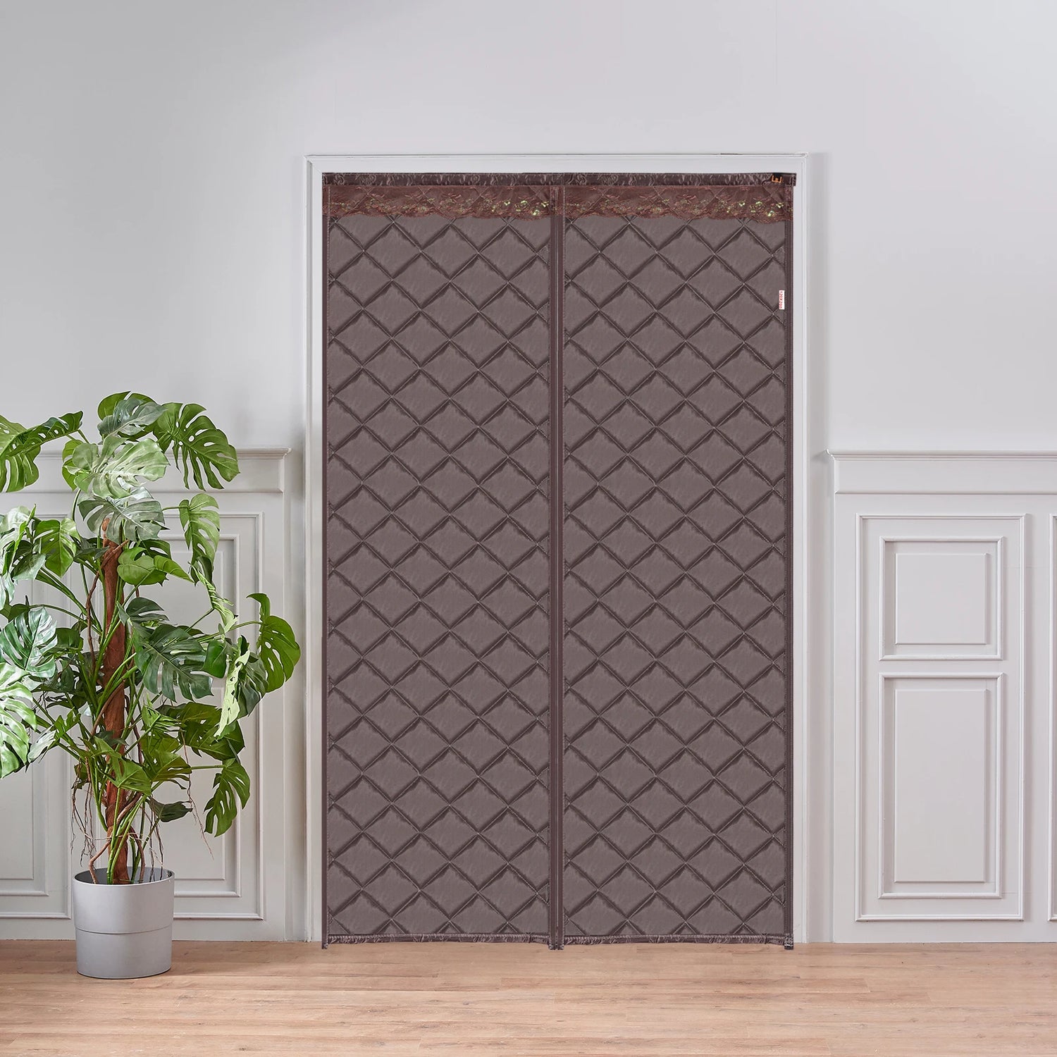Rideau de porte matelassé marron à motifs losanges, installé dans une pièce élégante avec une plante verte sur sol en bois clair.