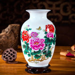 Un vase en porcelaine blanche décoré de fleurs épanouies aux couleurs vives, entourées de feuillages verdoyants et d'un papillon volant.